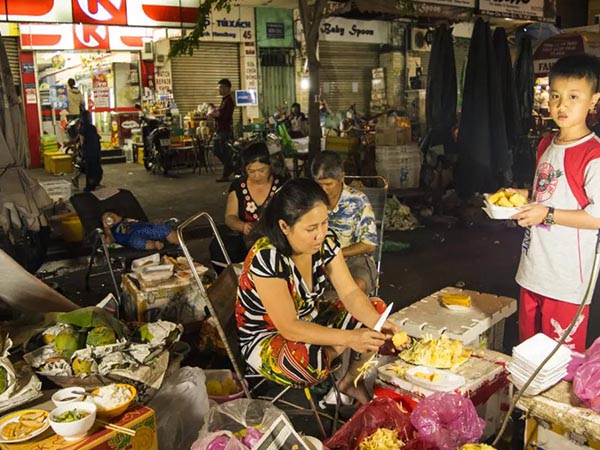 A woman sitting at an outdoor market with other people.