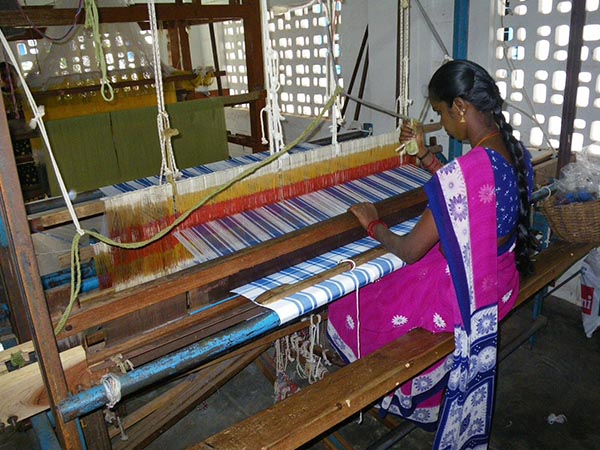 A woman in pink and blue dress weaving on a loom.