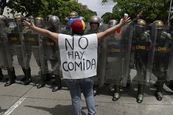 A person with a sign on his back stands in front of a group of police.