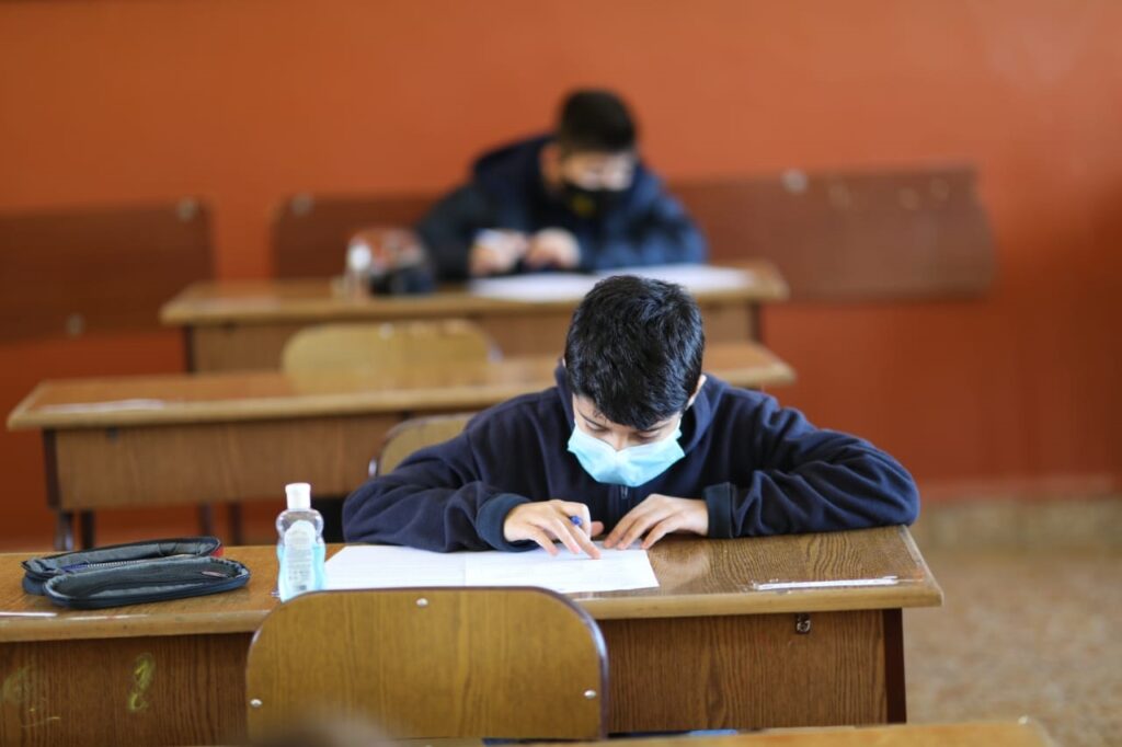 A boy wearing a mask is writing on paper.