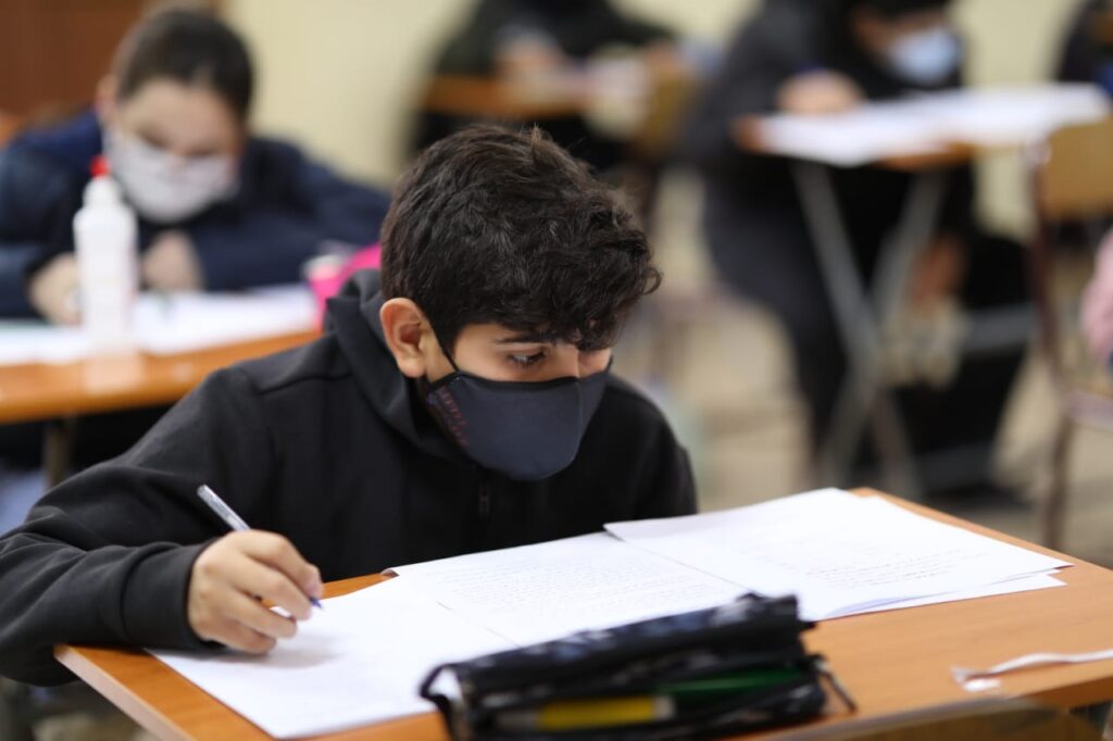 A boy wearing a mask is writing on paper.