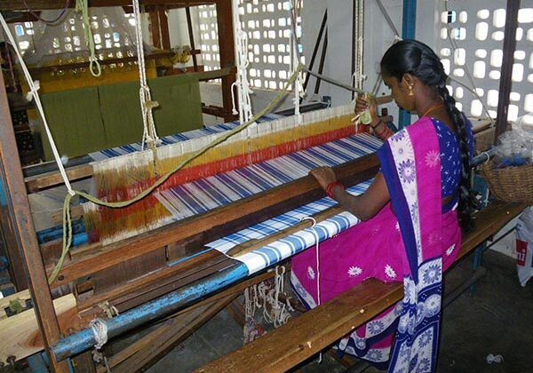 A woman in pink and blue dress weaving on a loom.